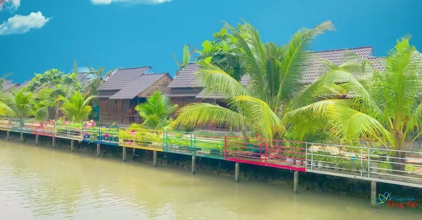 Dãy nhà gỗ homestay ven sông với lan can hoa nhiều màu tại Làng du lịch sinh thái Ông Đề