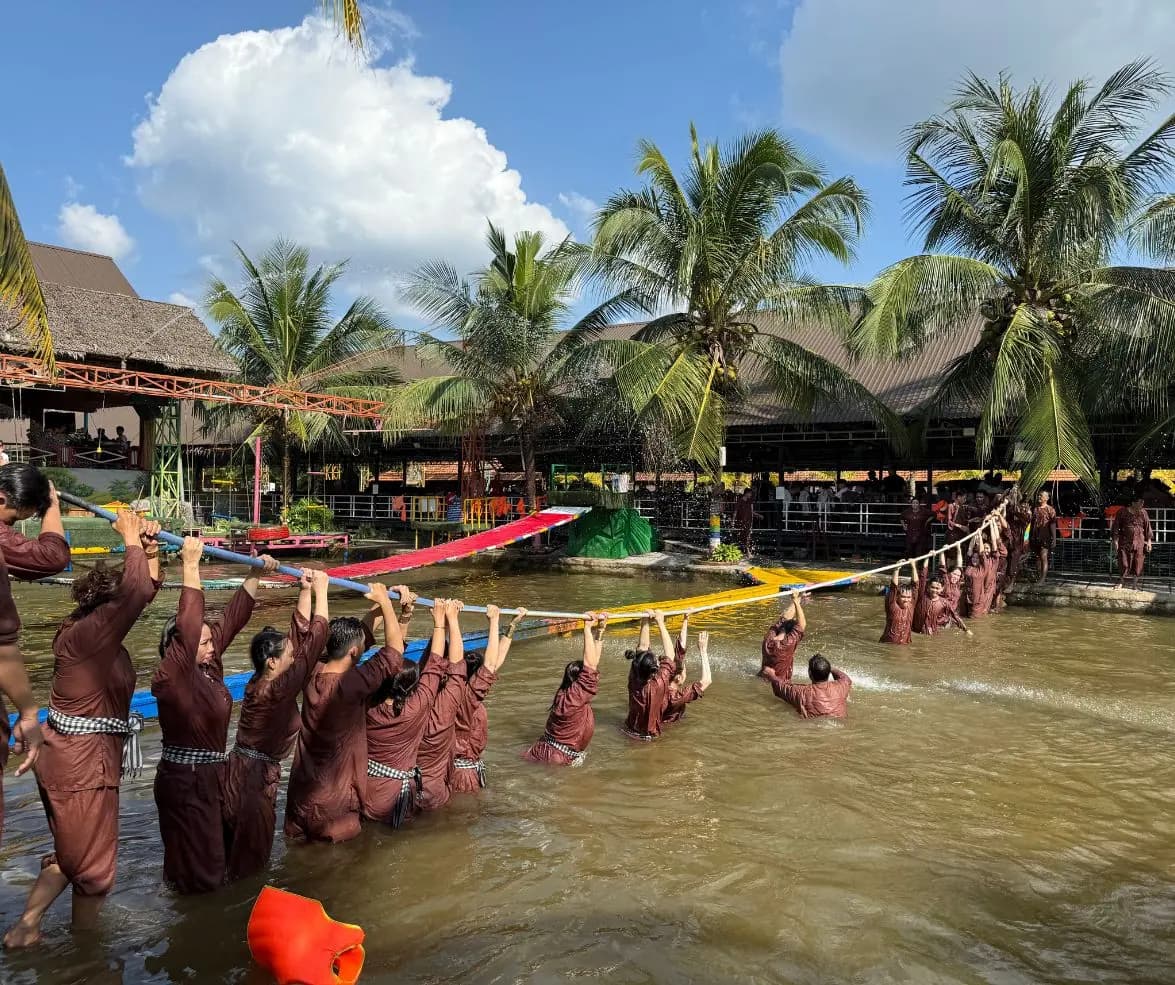 Du khách lội ao, hai tay bám thanh ngang treo trên dây để vượt qua mặt nước