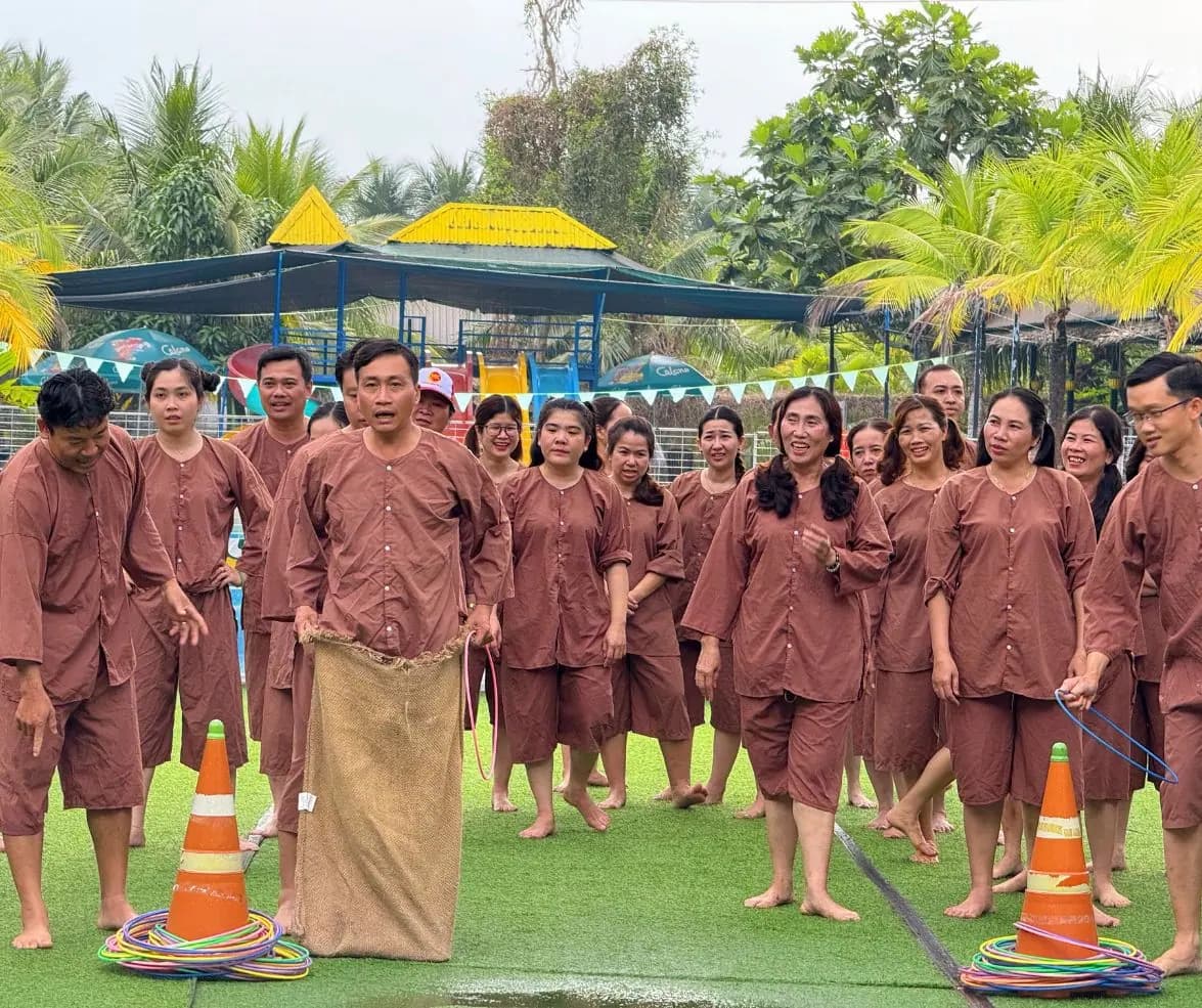 Du khách áo bà ba nâu nhảy bao bố trên sân cỏ, cả đoàn đứng hai bên cổ vũ